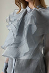 Close-up of a person wearing a light gray ruffled blouse against a neutral background.