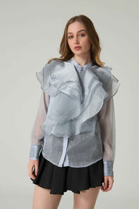 Woman wearing a sheer blouse with ruffled details on a plain background.