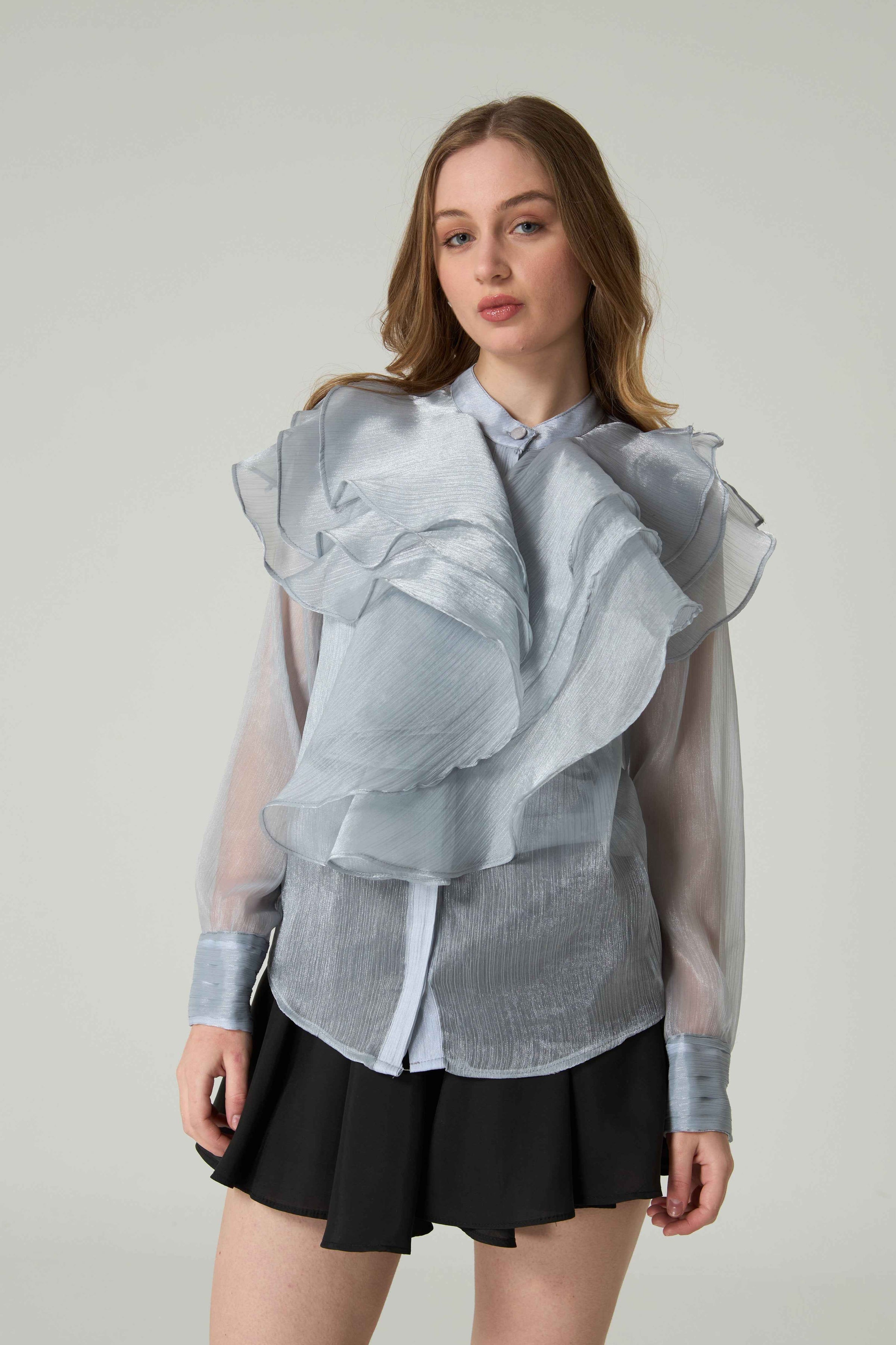 Woman wearing a sheer blouse with ruffled details on a plain background.