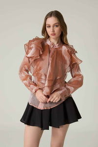 Woman wearing a sheer pink blouse with ruffles and a black skirt on a plain background.