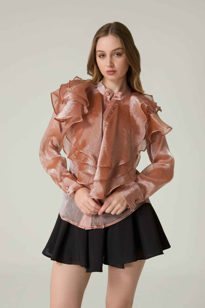 Woman wearing a sheer pink blouse with ruffles and a black skirt on a plain background.