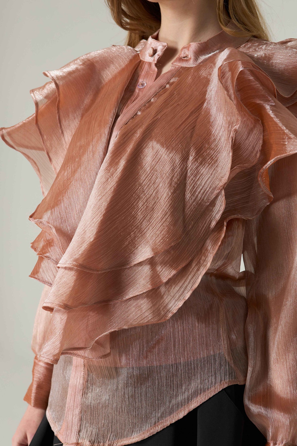 Pink ruffled blouse worn by a person on a light gray background.