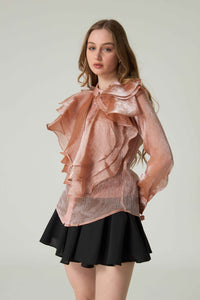 Woman wearing a sheer peach blouse with ruffles and a black skirt on a plain background.