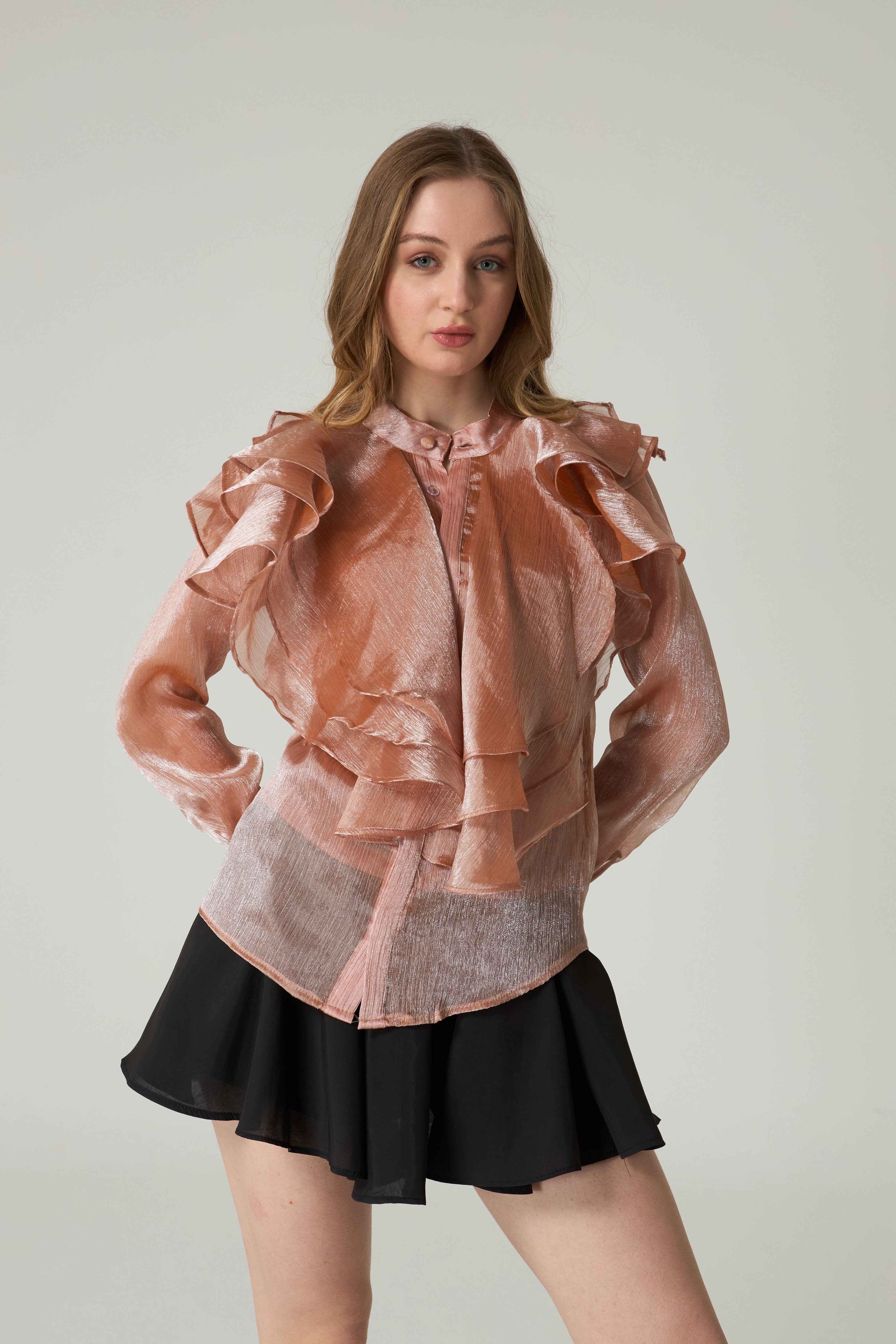 Woman wearing a sheer ruffled blouse over a black skirt on a plain background.