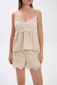 Woman wearing a cream lace top and shorts set on a white background.