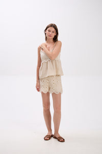 Woman wearing a beige top and lace shorts on a white background.