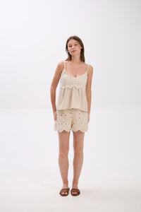 Woman wearing a beige lace top and shorts on a white background.