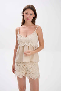 Woman wearing a beige lace camisole and shorts set on a white background.