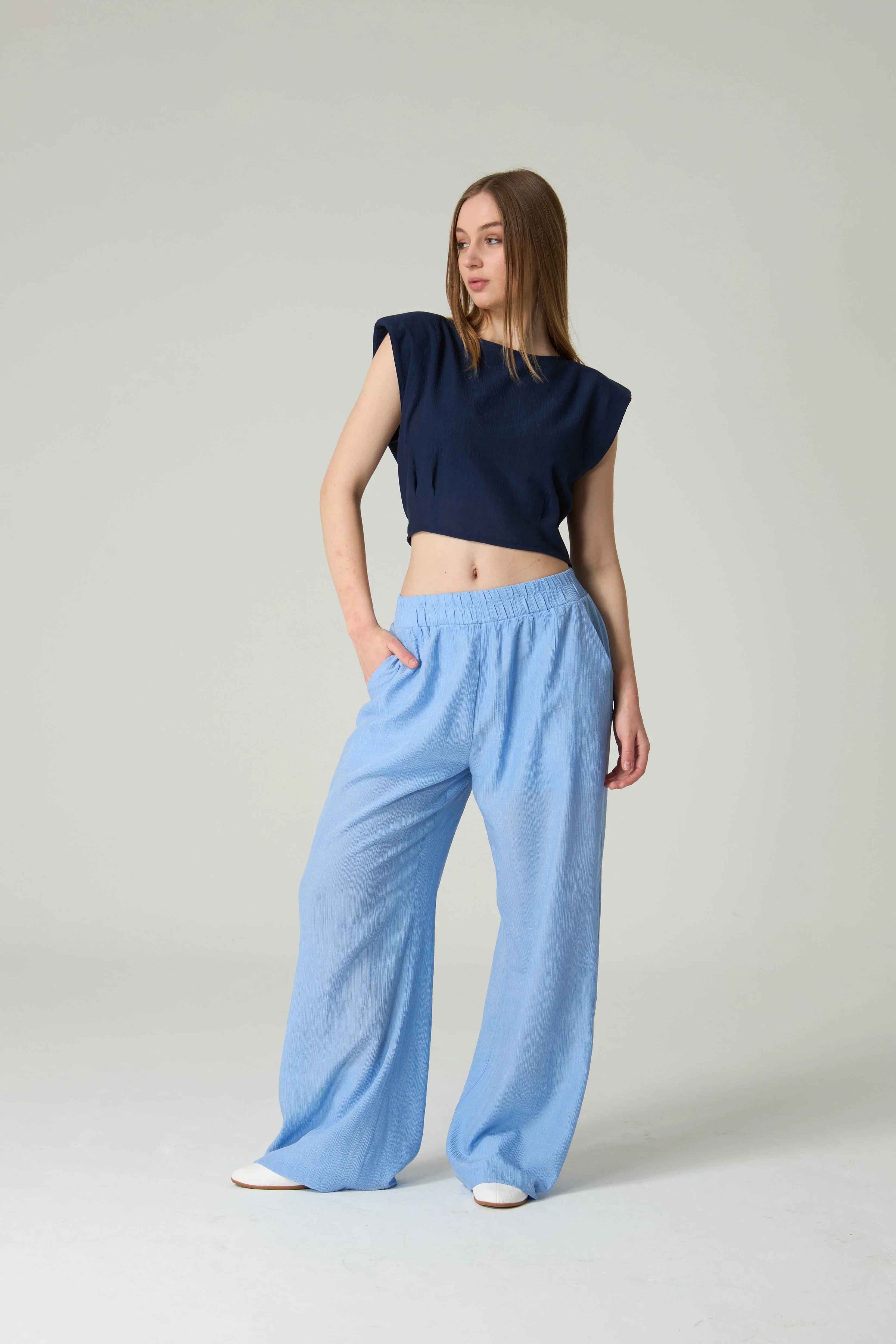 Woman wearing a navy top and light blue pants on a plain background.