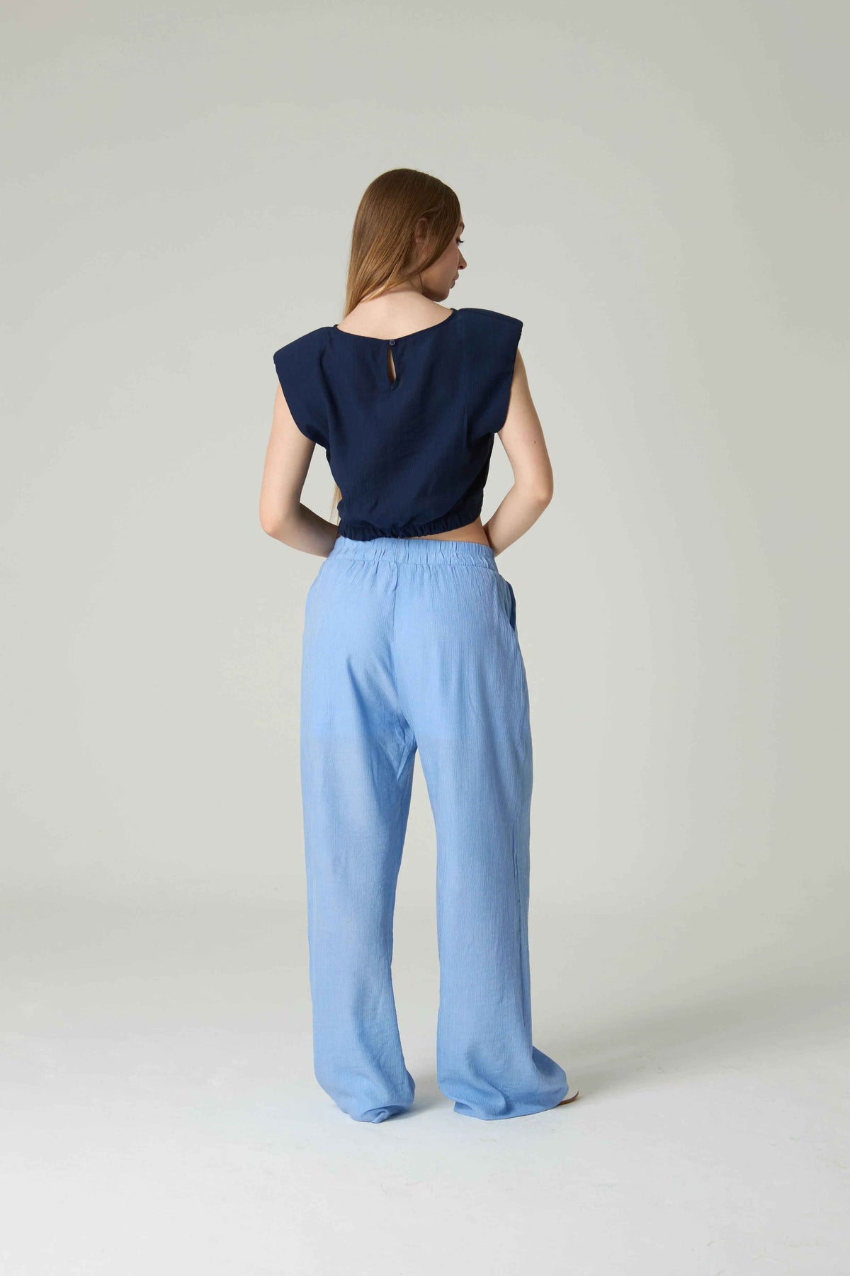 Woman wearing a navy top and light blue pants on a plain background.