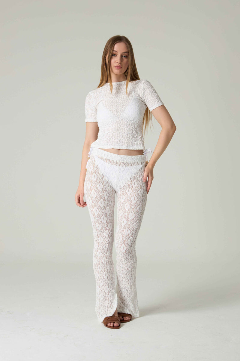 Woman wearing a white lace outfit on a plain background.