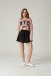 Woman wearing a pink 'NYC' sweater and black skirt on a plain background.