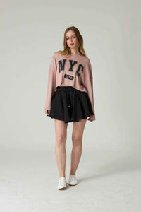 Woman wearing a pink 'NYC' sweatshirt and black skirt on a white background.