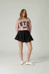 Woman wearing a pink 'NYC' sweater and black skirt on a white background.