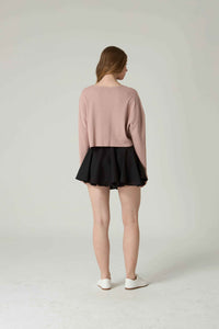 Person wearing a pink sweater and black skirt on a plain background.
