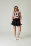 Woman wearing a pink 'NYC' sweatshirt and black skirt on a white background.