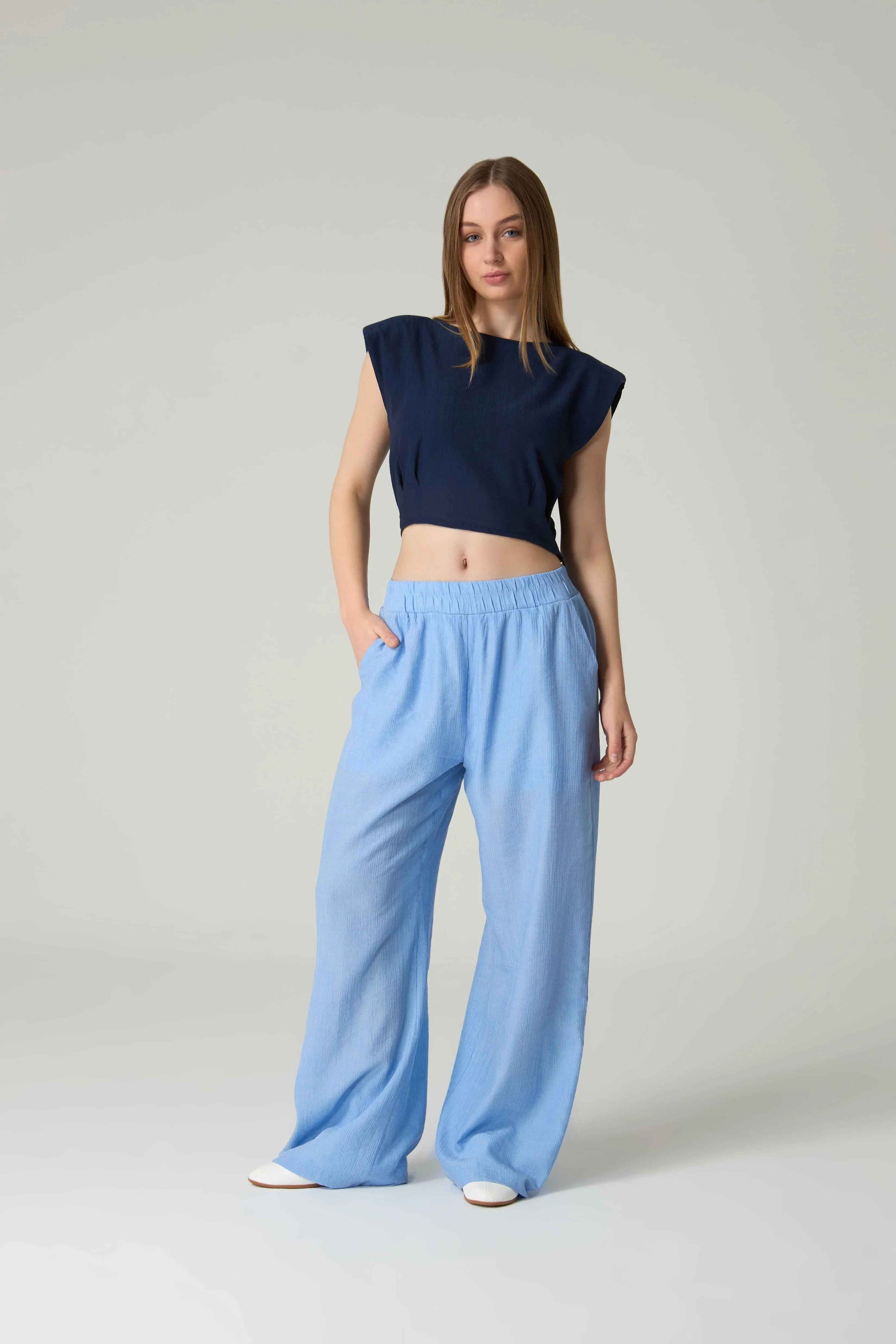 Woman wearing a navy top and light blue pants on a plain background.