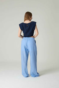 Woman wearing a navy top and light blue pants on a plain background.