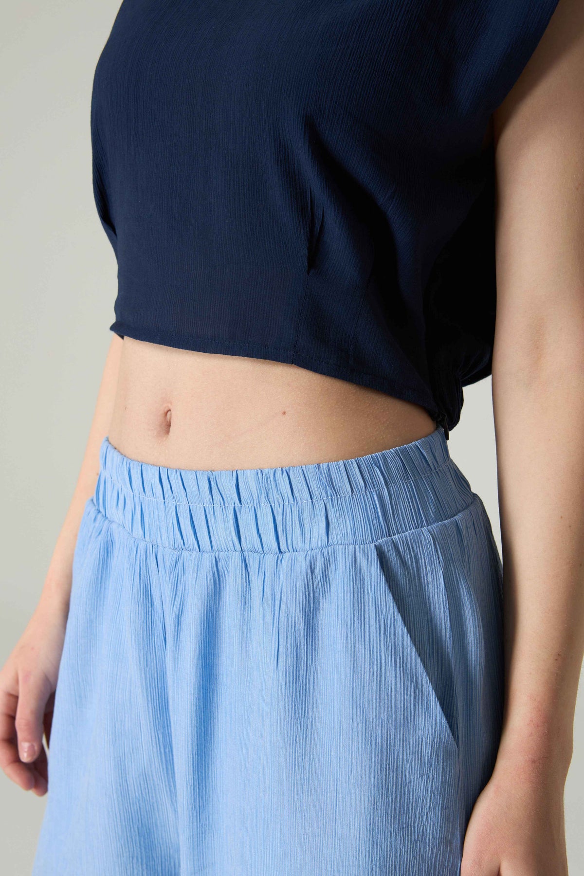 Person wearing a navy top and light blue pants against a neutral background.