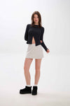 Woman wearing a black sweater and beige skirt on a white background.