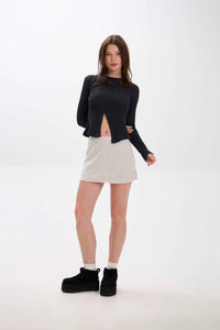 Woman wearing a black sweater and beige skirt on a white background.
