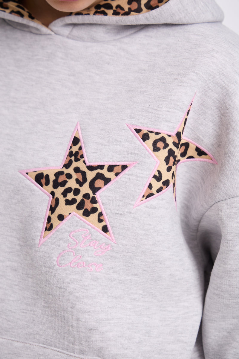 Close-up of a light grey hoodie featuring two leopard print star patches outlined in pink stitching with the words “Stay Close” embroidered in pink thread beneath the design.