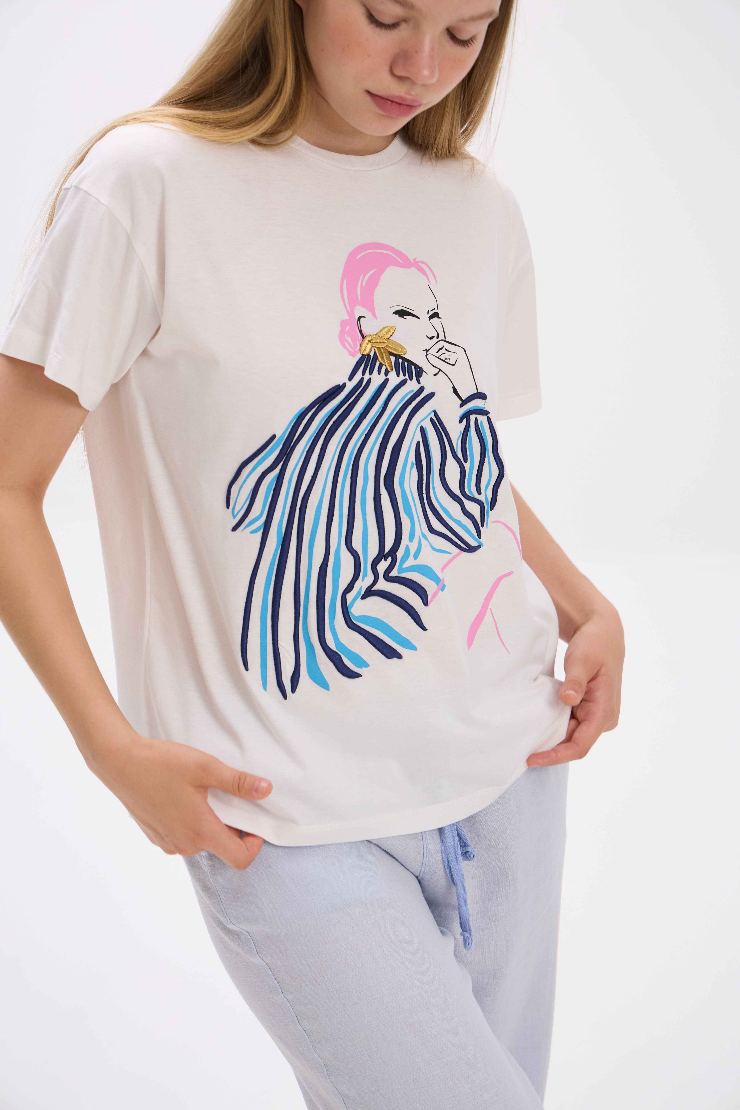 Person wearing a white t-shirt with a colorful graphic design on a plain background.