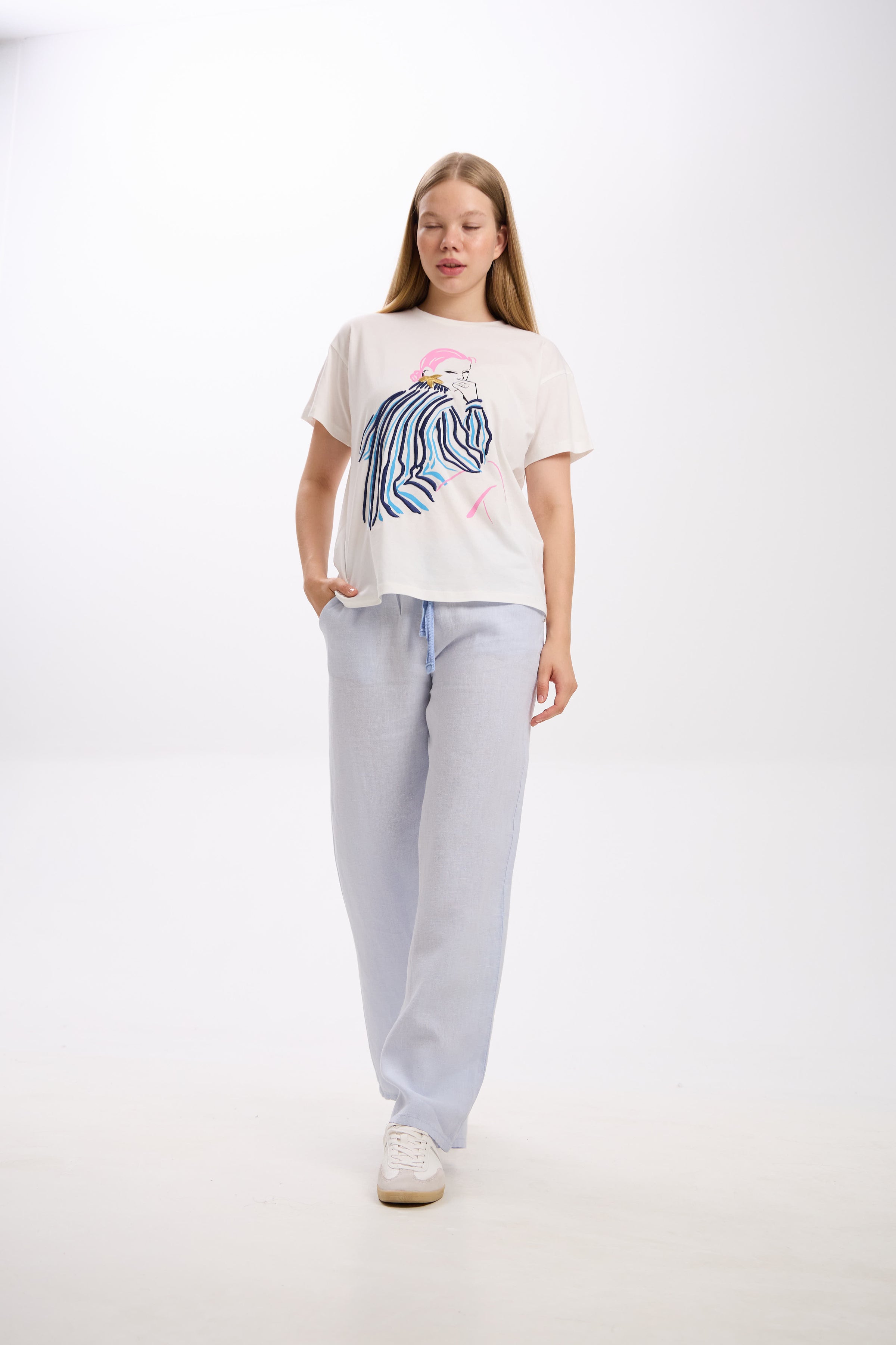 Woman wearing a white t-shirt with a graphic design and light gray sweatpants on a white background.