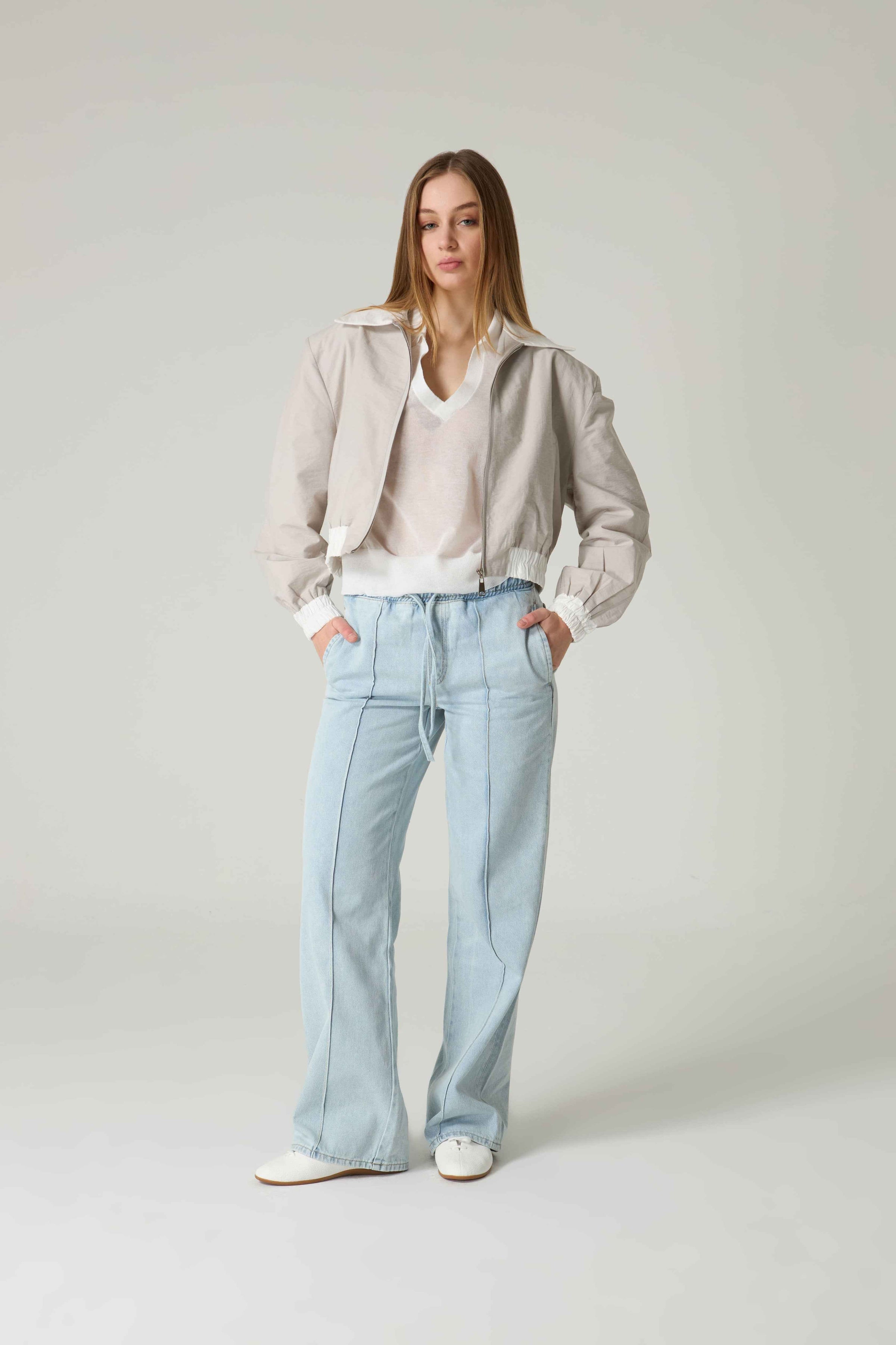 Woman wearing a light-colored jacket and jeans on a plain background.