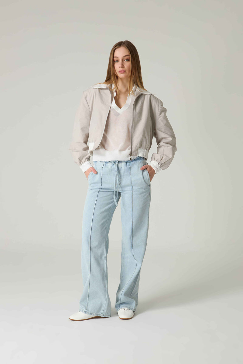 Woman wearing a light-colored jacket and jeans on a plain background.