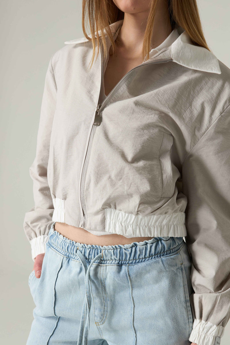 Person wearing a light gray jacket and light blue jeans against a neutral background.
