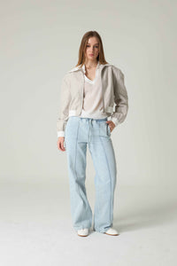 Woman wearing a beige blouse and light blue jeans on a plain background.