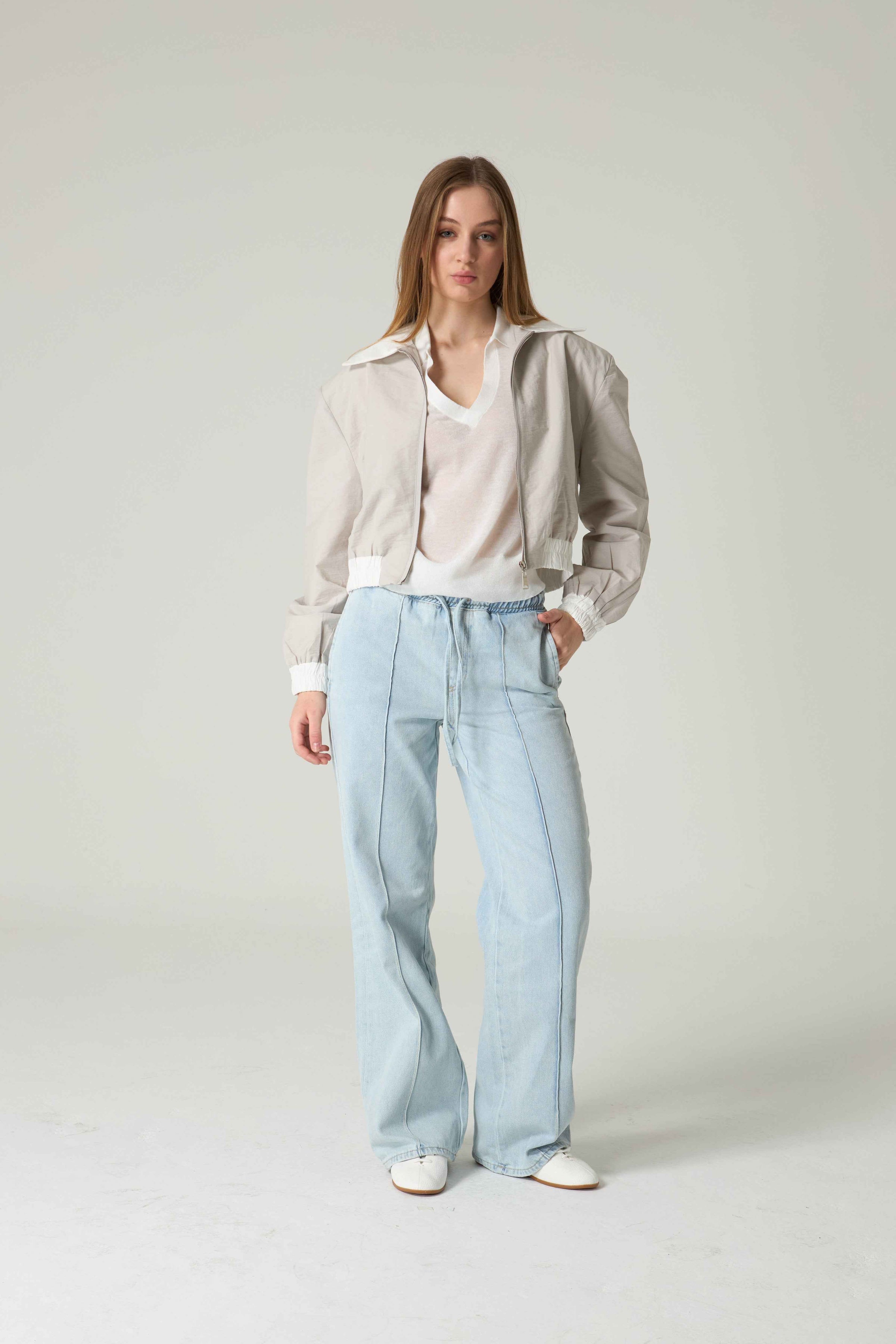 Woman wearing a beige blouse and light blue jeans on a plain background.