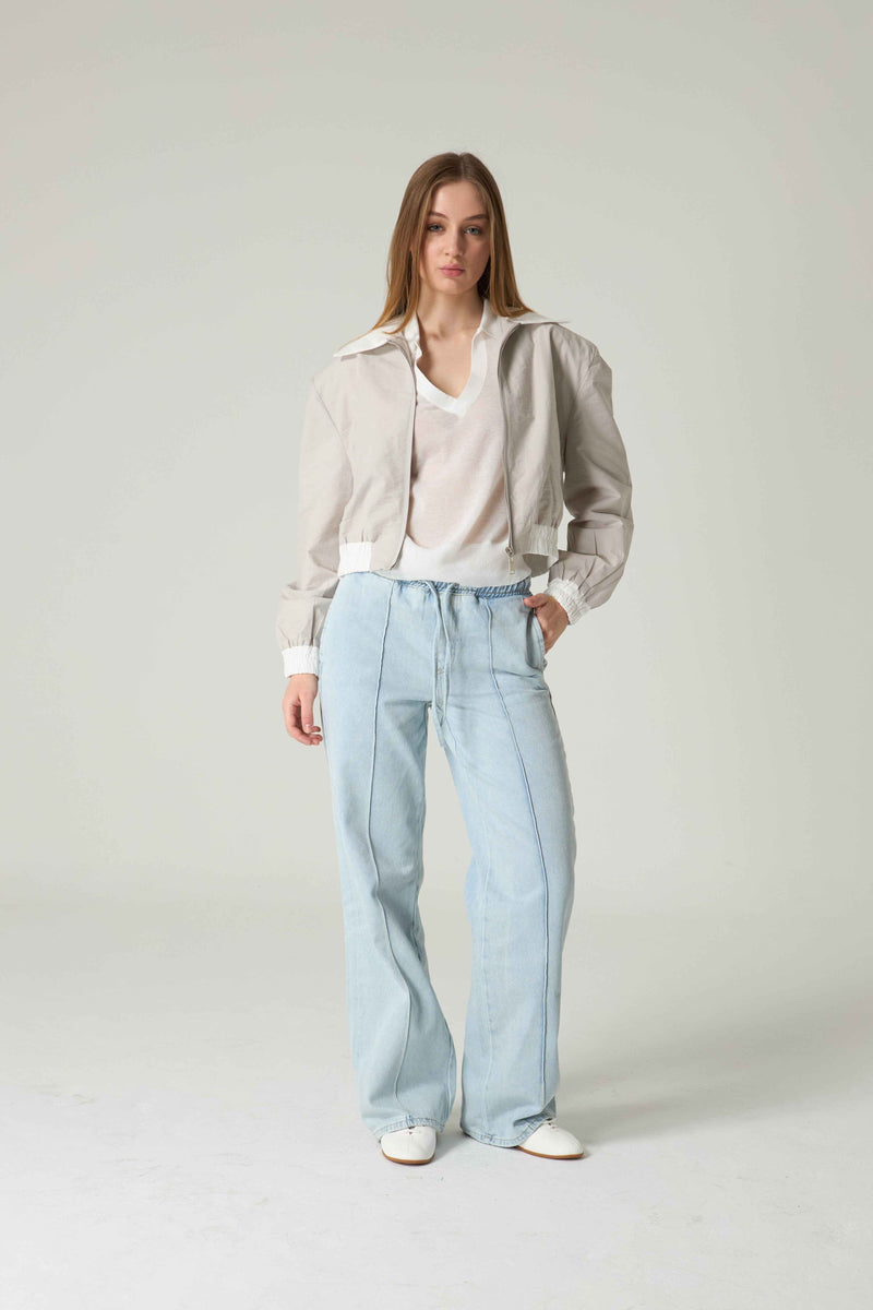 Woman wearing a beige blouse and light blue jeans on a plain background.