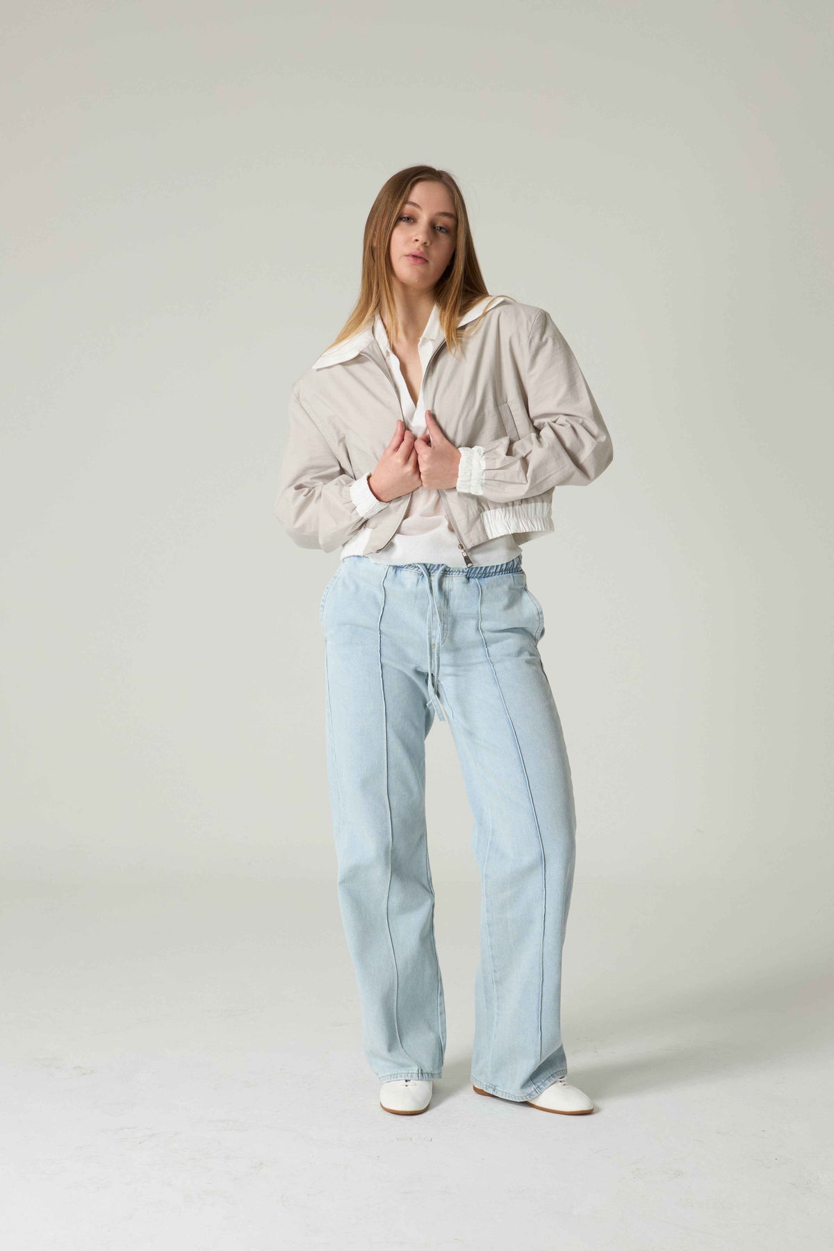 Person wearing a light-colored jacket and light blue jeans on a plain background.