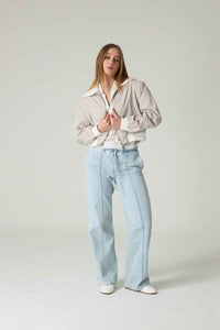 Person wearing a light-colored jacket and light blue jeans on a plain background.