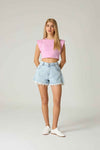 Woman wearing a pink crop top and light blue denim shorts on a plain background.