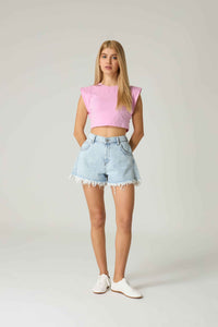 Woman wearing a pink crop top and light blue denim shorts on a plain background.