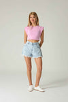 Person wearing a pink crop top and light blue denim shorts on a plain background.