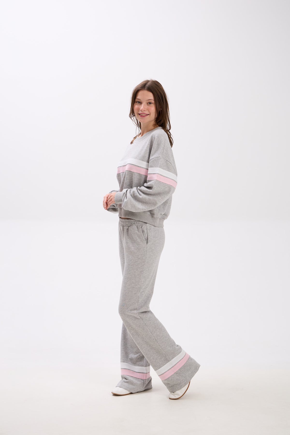 Person wearing a gray tracksuit with pink accents on a white background.