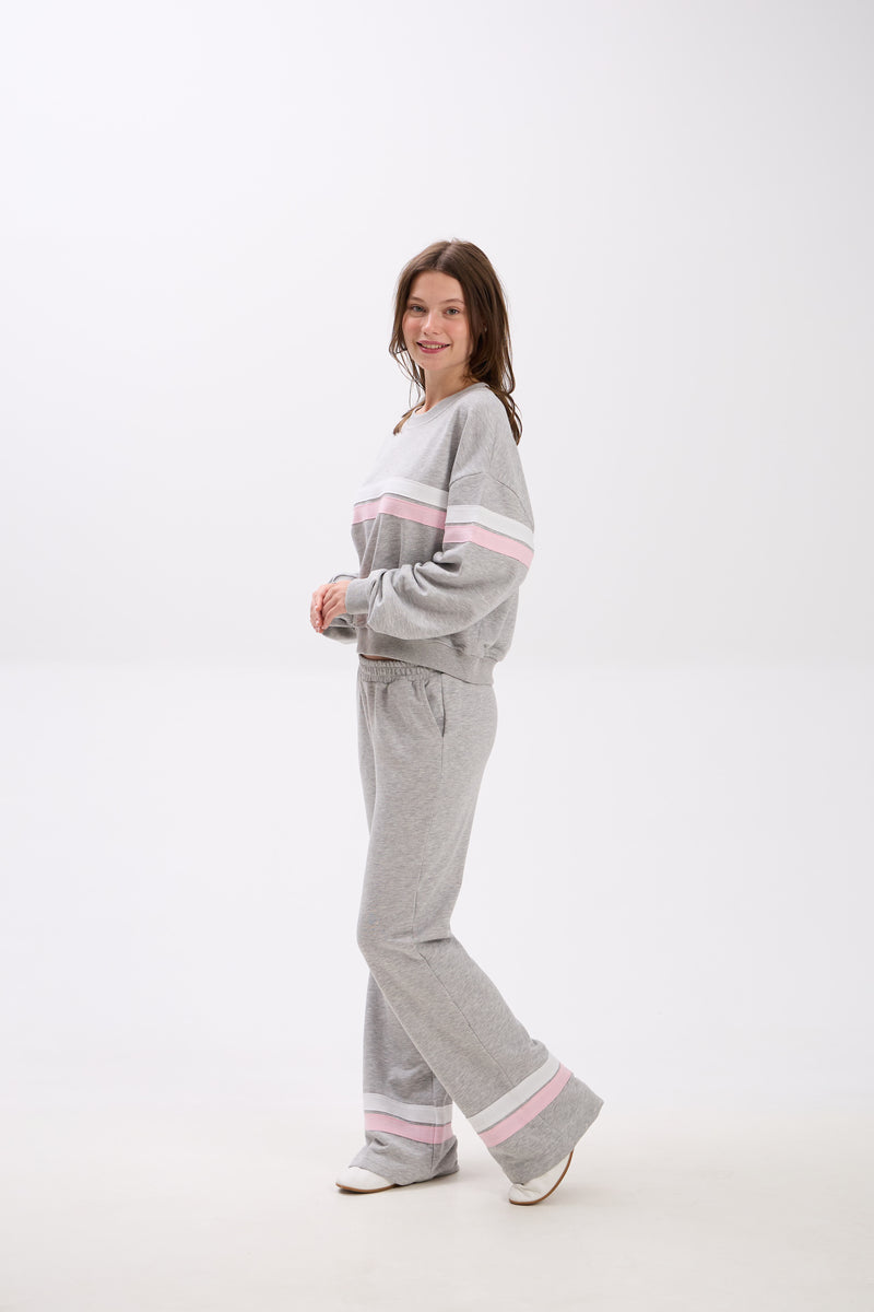 Person wearing a gray tracksuit with pink accents on a white background.