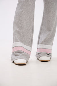 Gray sweatpants with pink bands worn by a person on a white background.