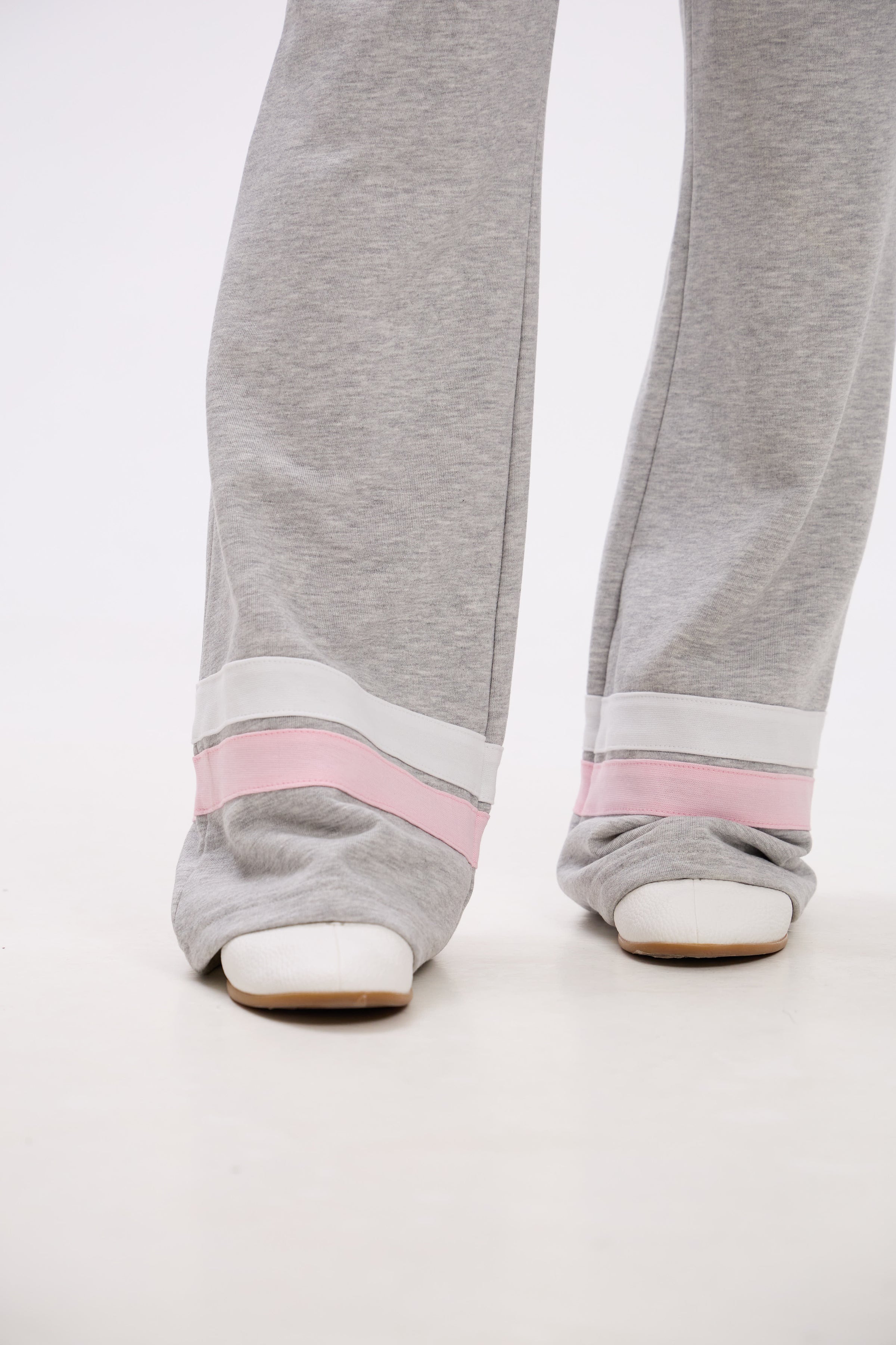 Gray sweatpants with pink bands worn by a person on a white background.