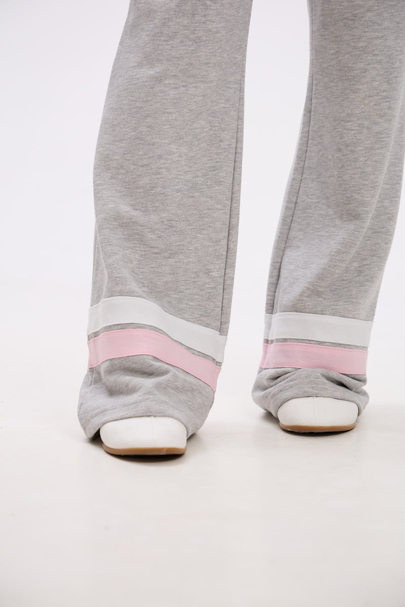Gray sweatpants with pink bands worn by a person on a white background.