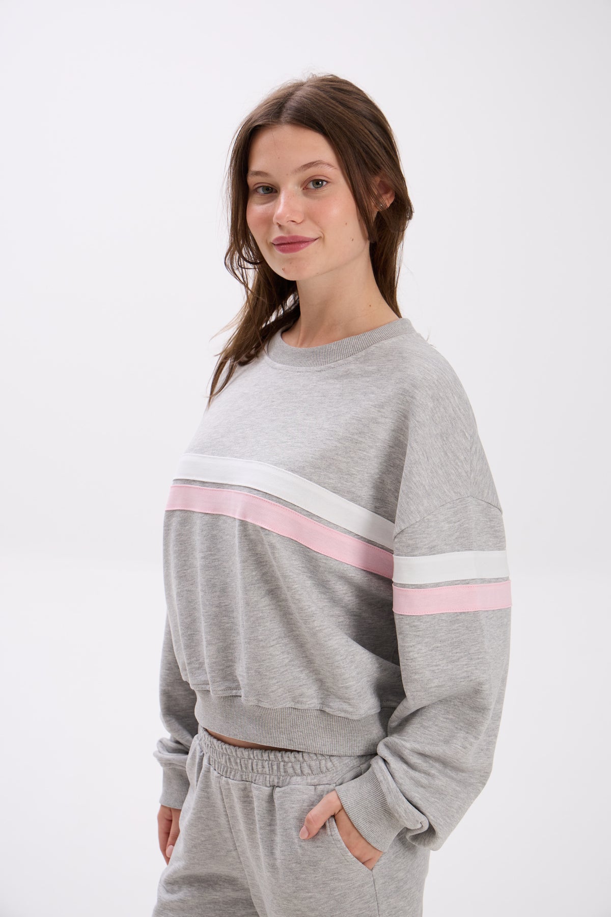 Woman wearing a gray sweatshirt with pink and white stripes on a white background.