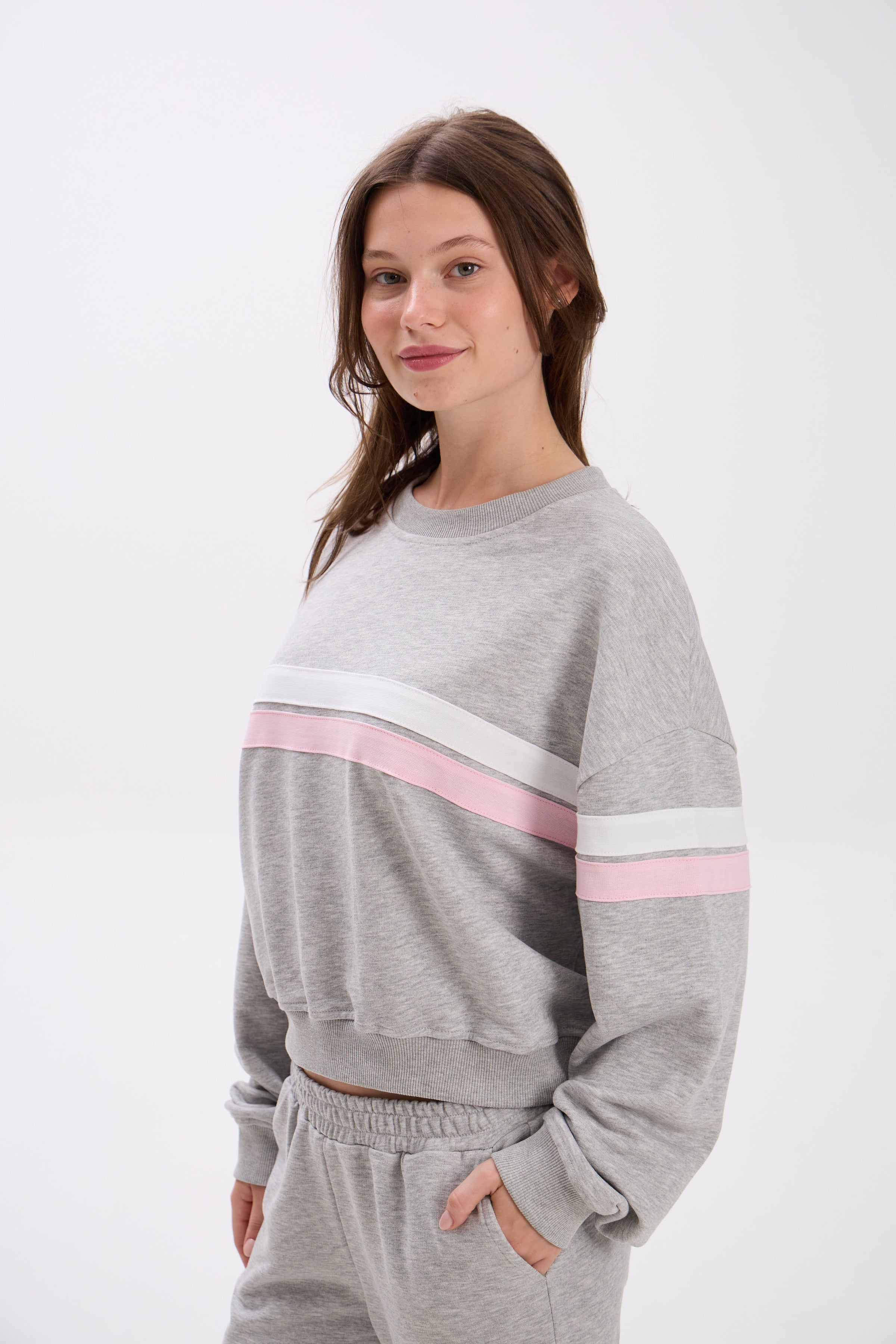 Woman wearing a gray sweatshirt with pink and white stripes on a white background.