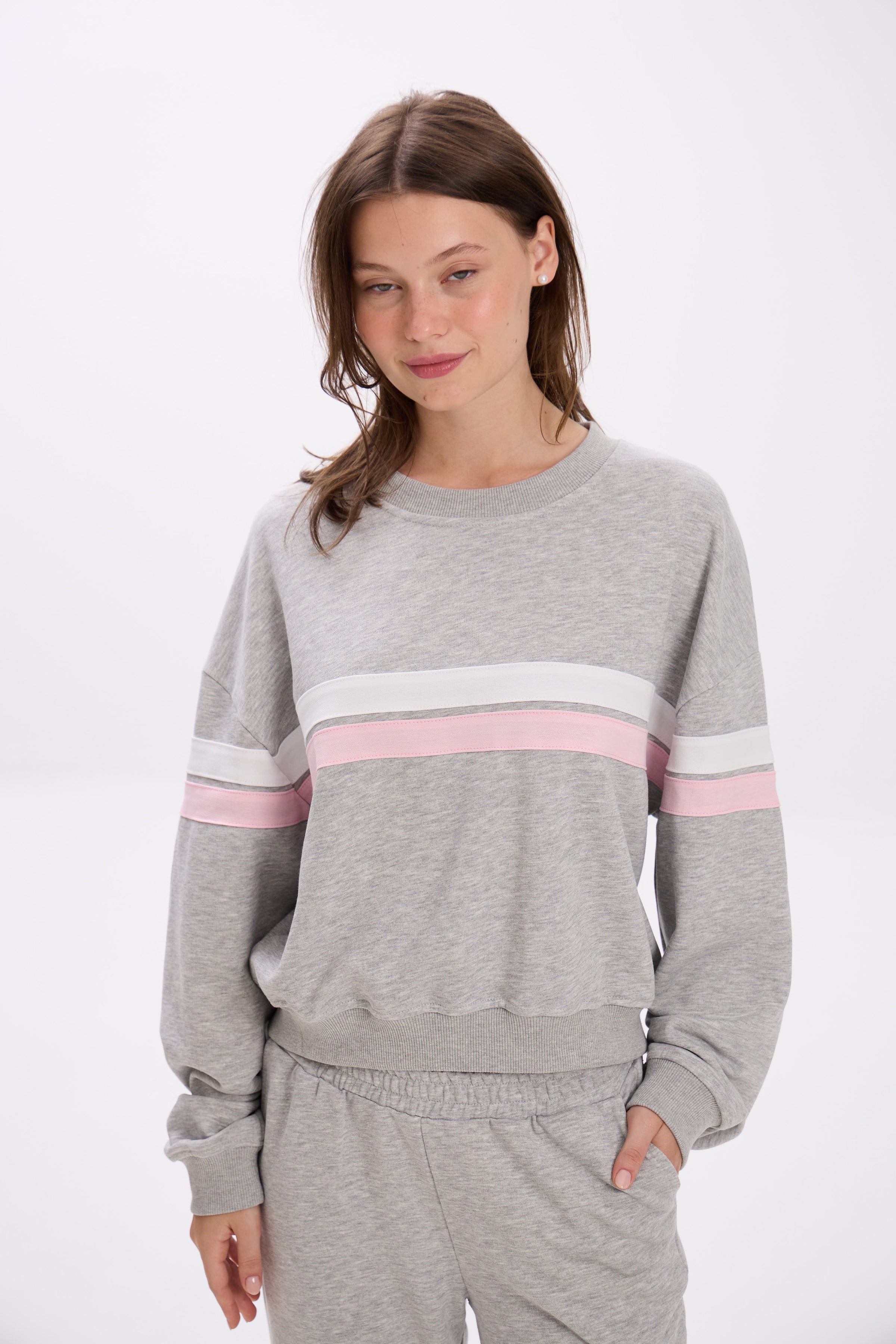 Woman wearing a gray sweatshirt with pink and white stripes on a white background.