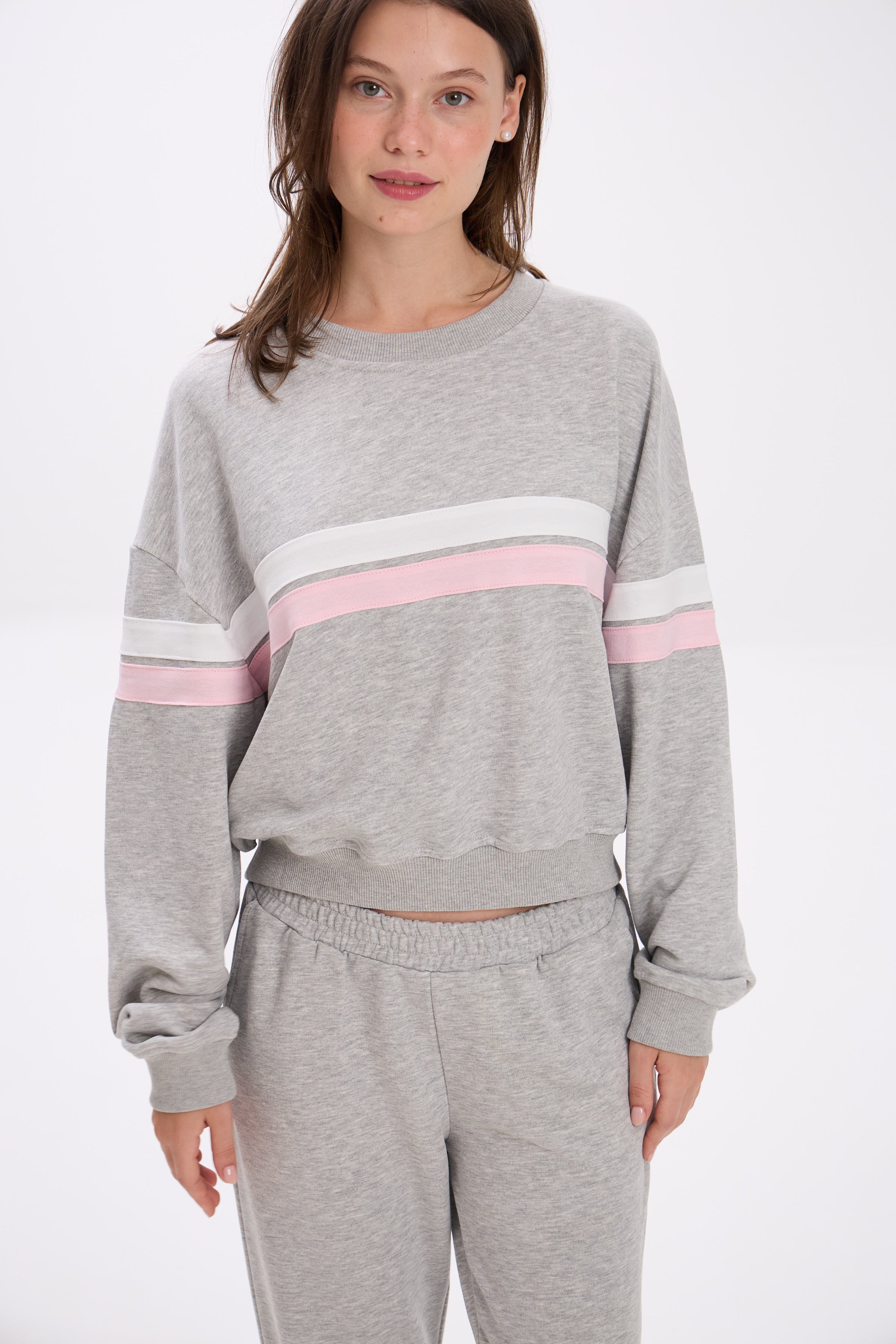 Woman wearing a gray sweatshirt with pink and white stripes on a white background.
