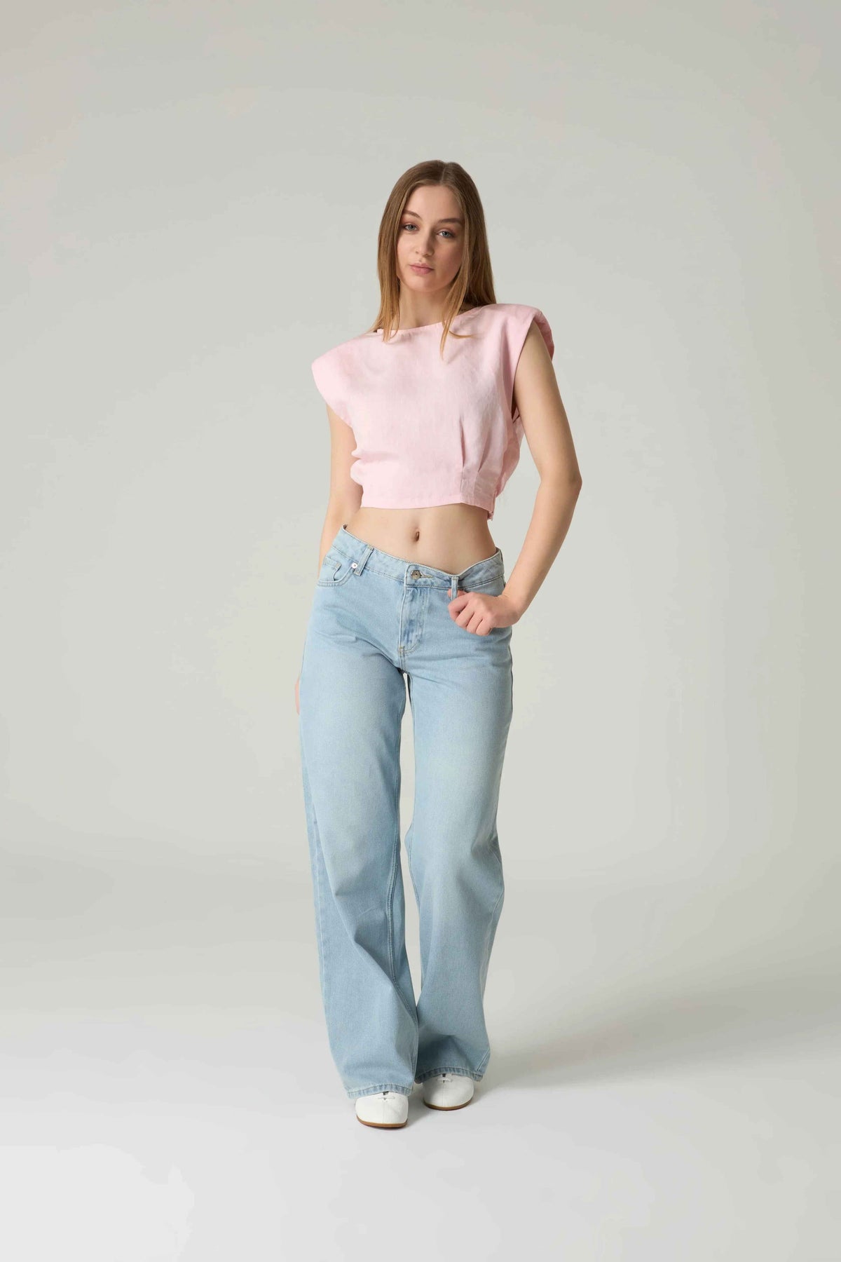 Woman wearing a pink sleeveless top and light blue jeans on a white background.