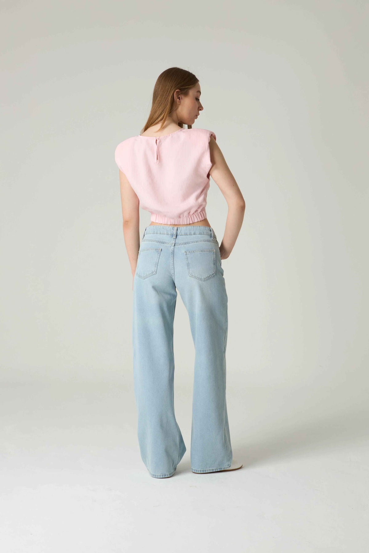 Woman wearing a pink top and light blue jeans on a white background.